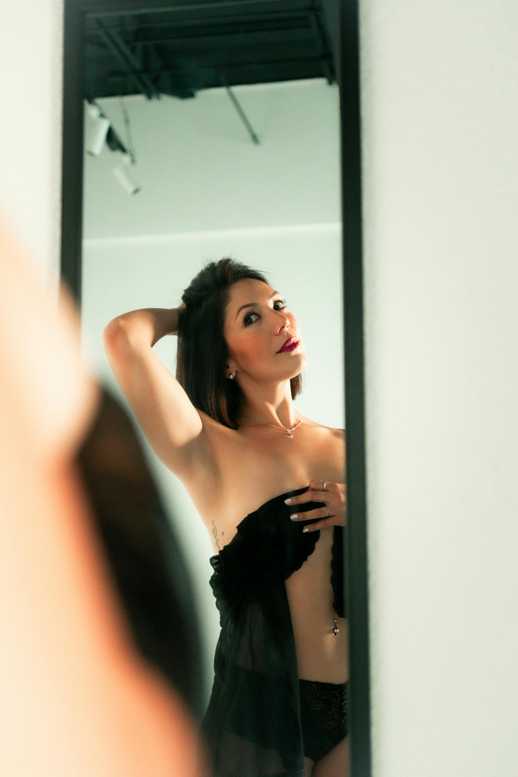 A glamorous woman in elegant attire poses confidently in front of a mirror indoors.