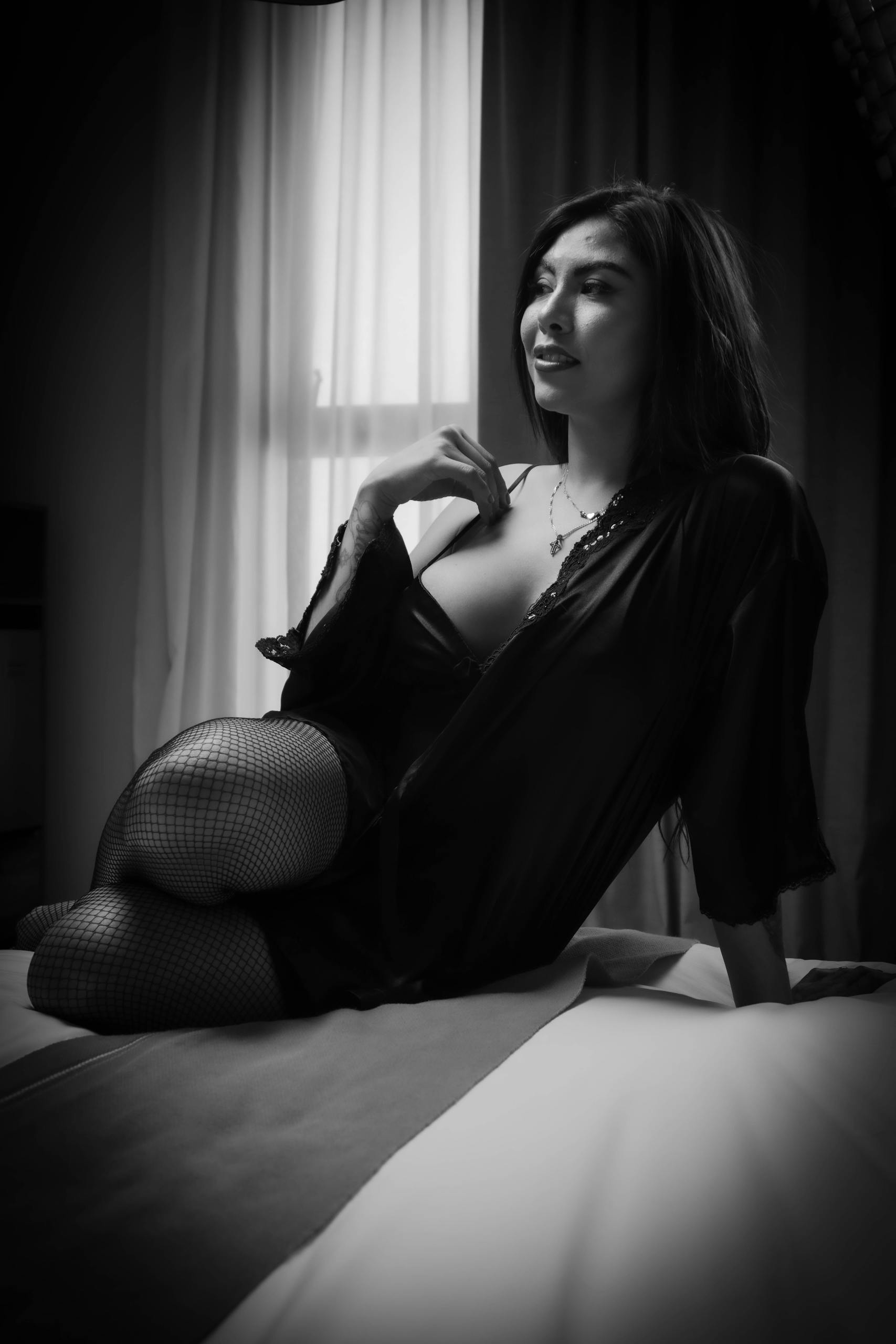 Black and white portrait of a woman in stylish attire, seated in a room with soft lighting.