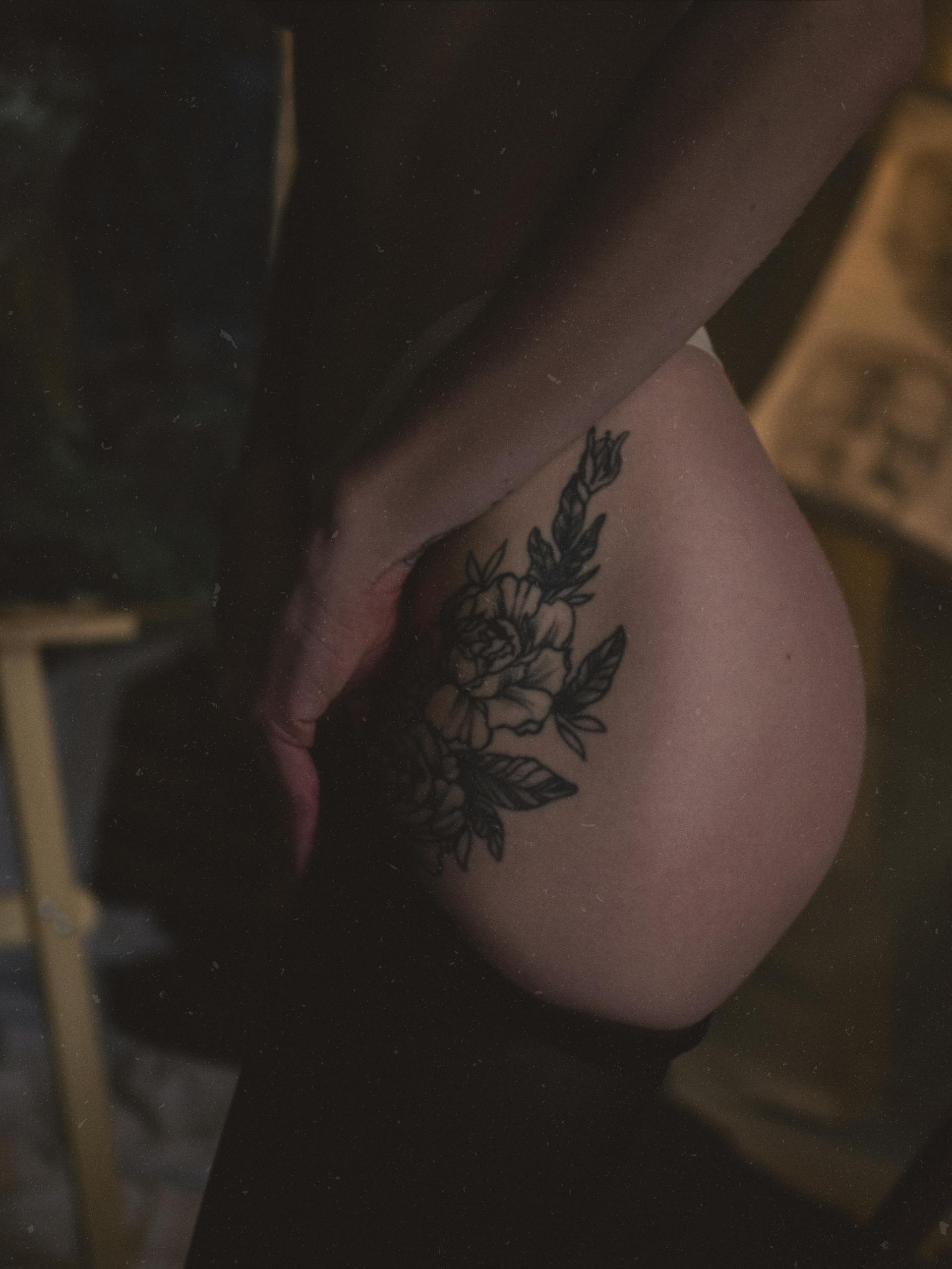 Intimate closeup of a woman with a floral hip tattoo in soft dim lighting.